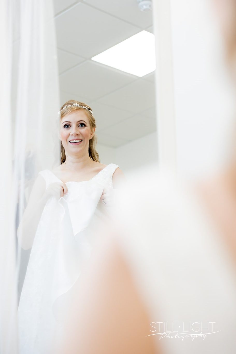 Bride smiling while holding her wedding dress, preparing for the ceremony.
